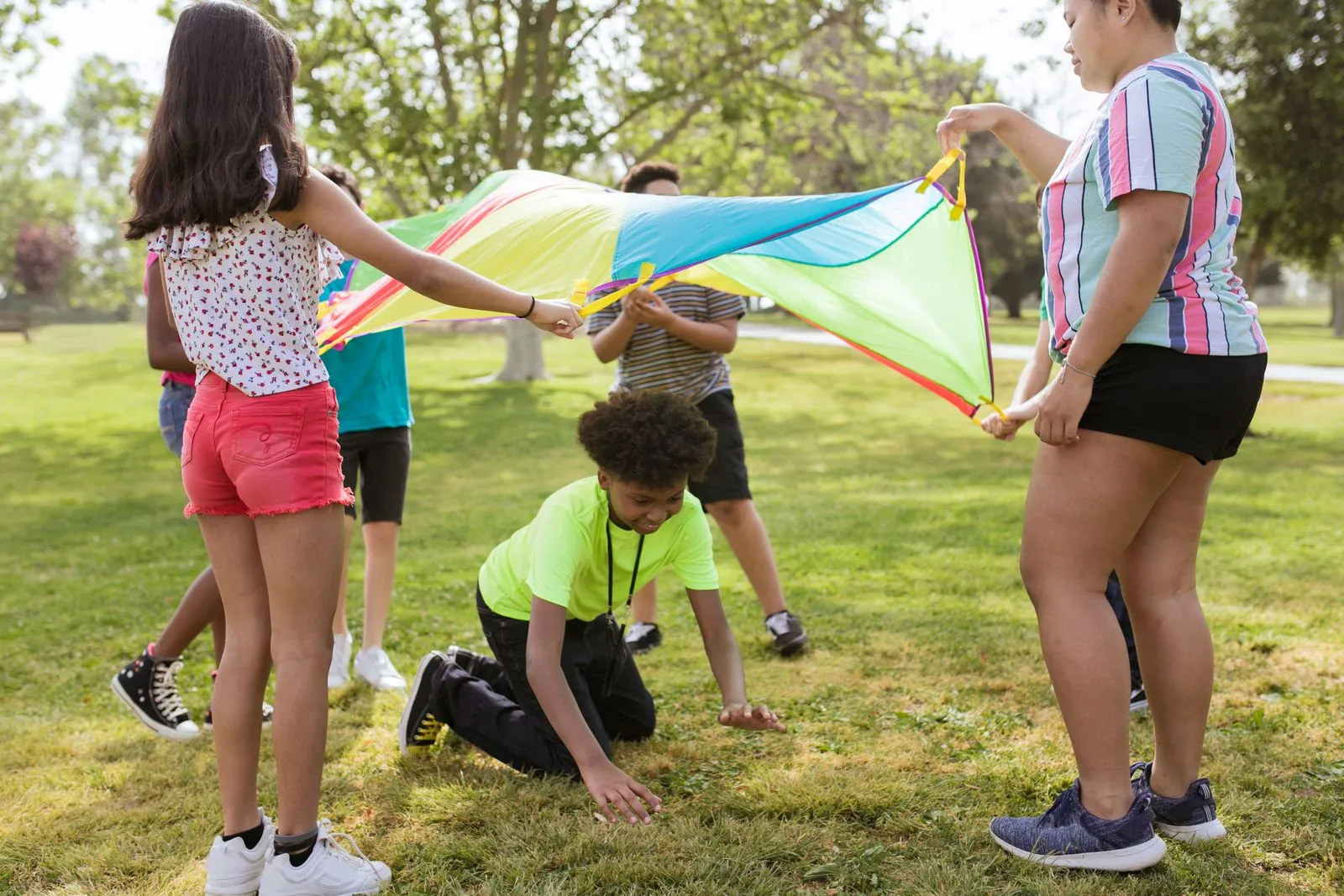 Infants jugant amb un paracaigudes de colors a l'aire lliure en una activitat de grup del casal d'estiu